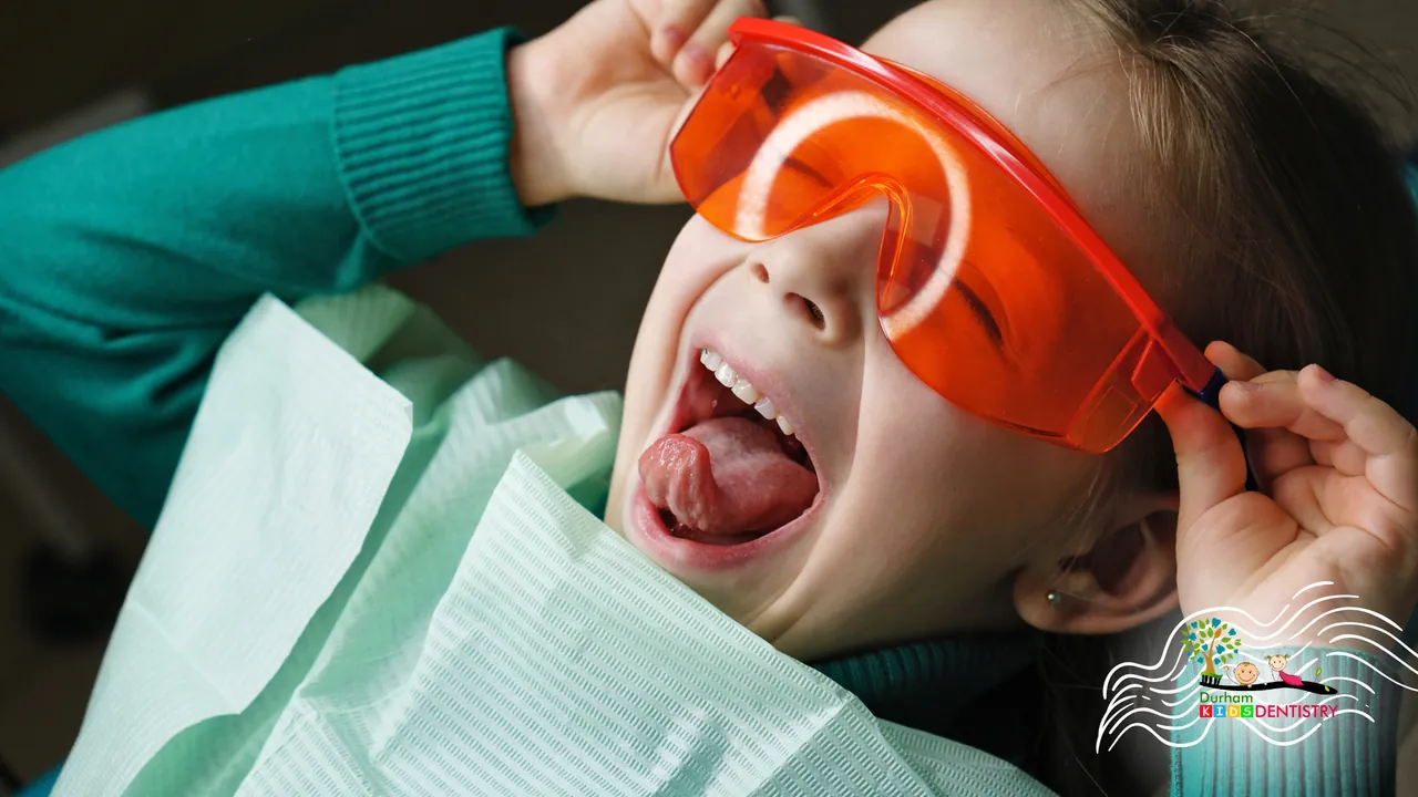 A little girl is sitting in a dental chair wearing safety glasses.